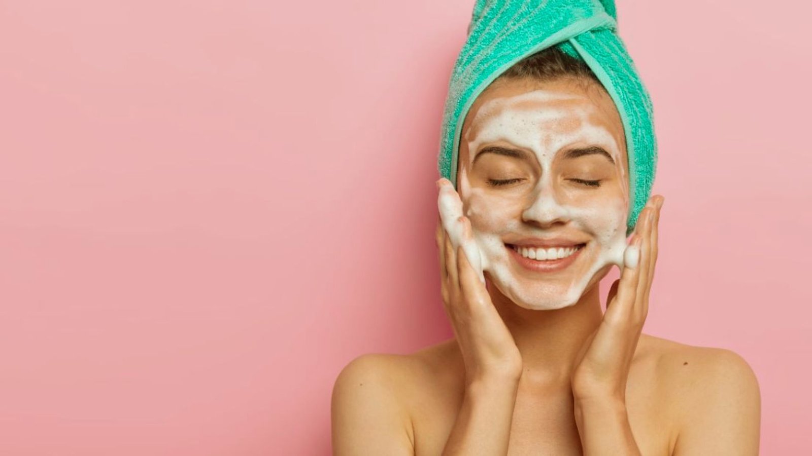 A woman with a towel on her head applies a face mask, relaxing in a spa-like setting.