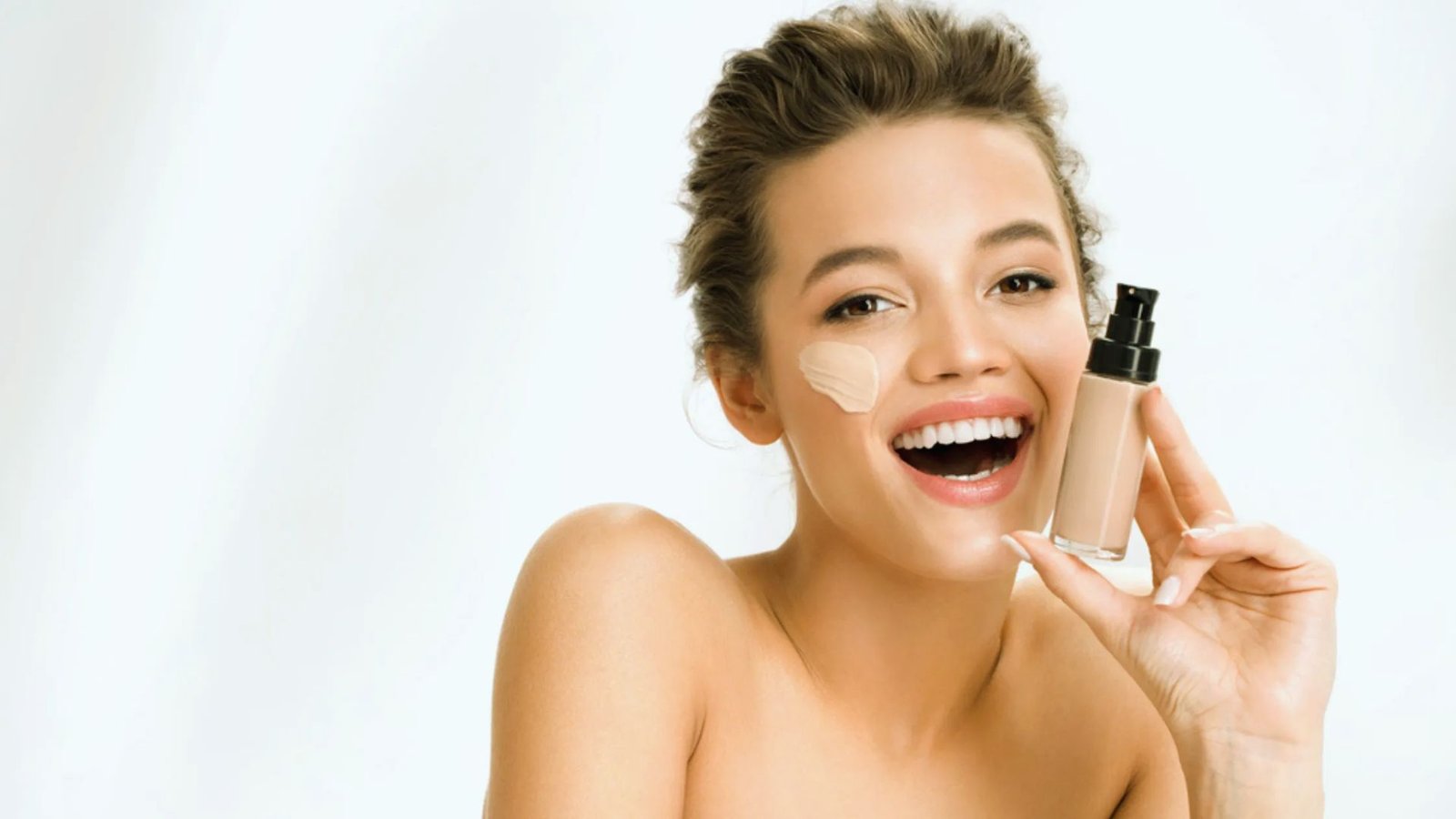 A smiling woman holds a bottle of foundation, showcasing her enthusiasm for beauty products.