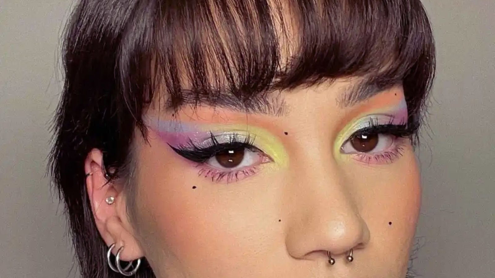 A woman with vibrant makeup and multiple piercings, showcasing a bold and artistic personal style.