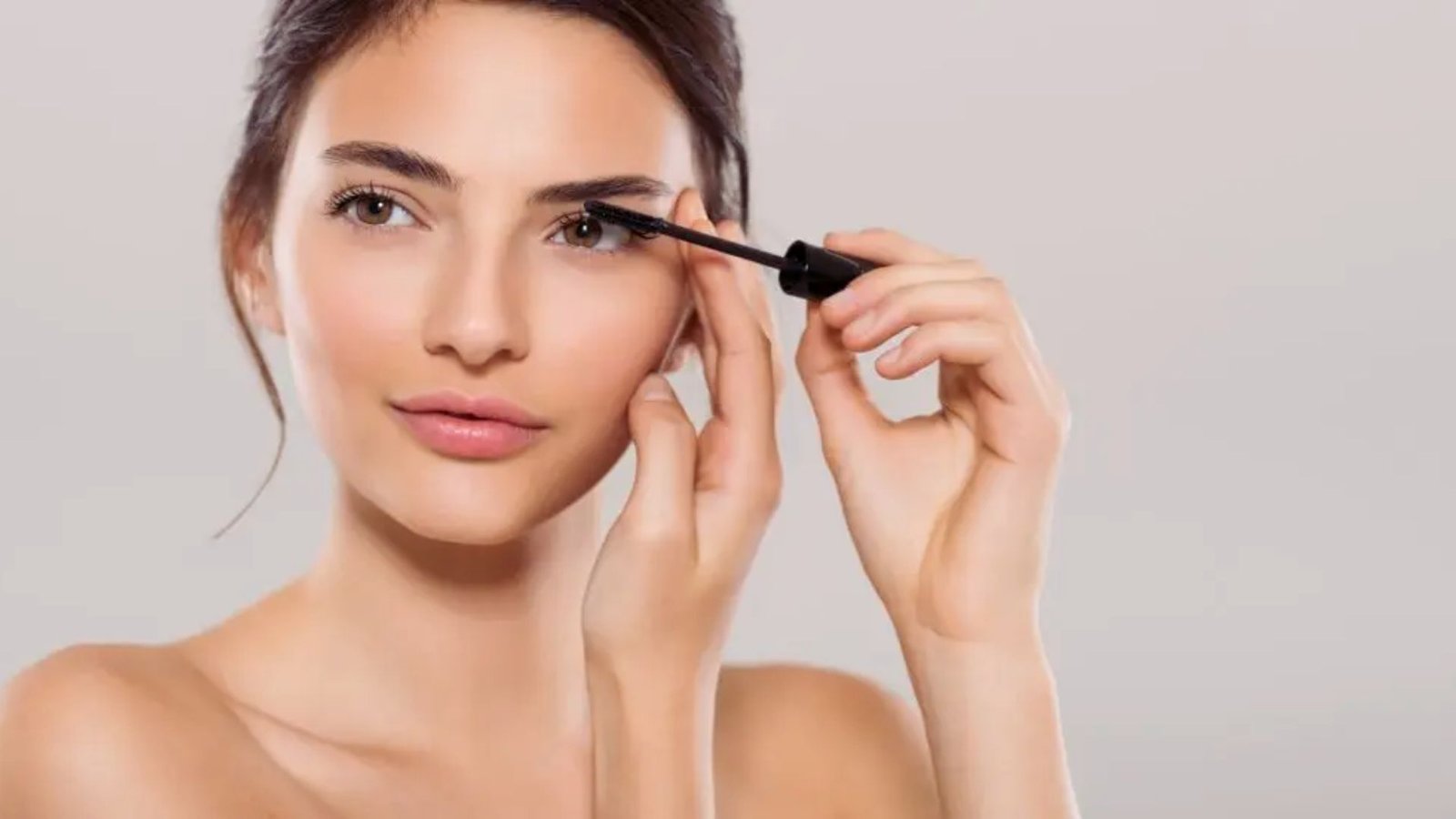 A woman carefully applies mascara to enhance her eyelashes in front of a mirror.