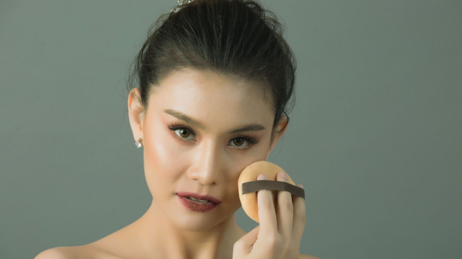 A woman applying a sponge to her face, likely for makeup or skincare purposes.