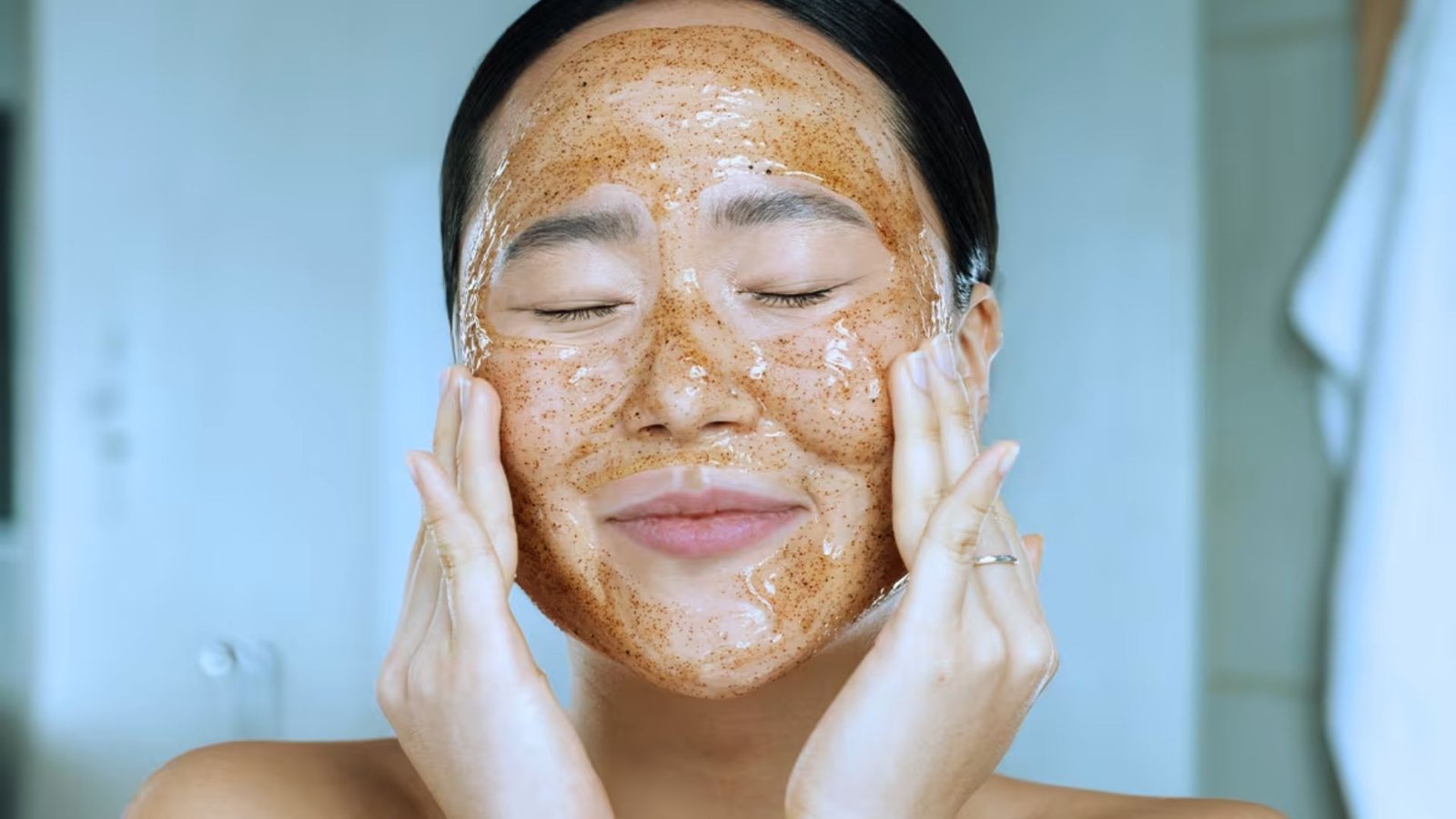 A woman with brown skin applies a facial mask, focusing on her skincare routine.