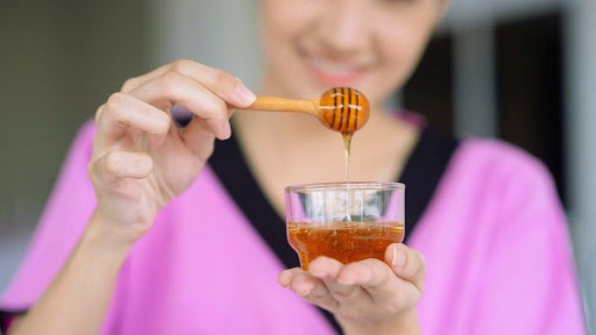 A woman holds a spoon filled with golden honey, poised to drizzle it into a bowl.