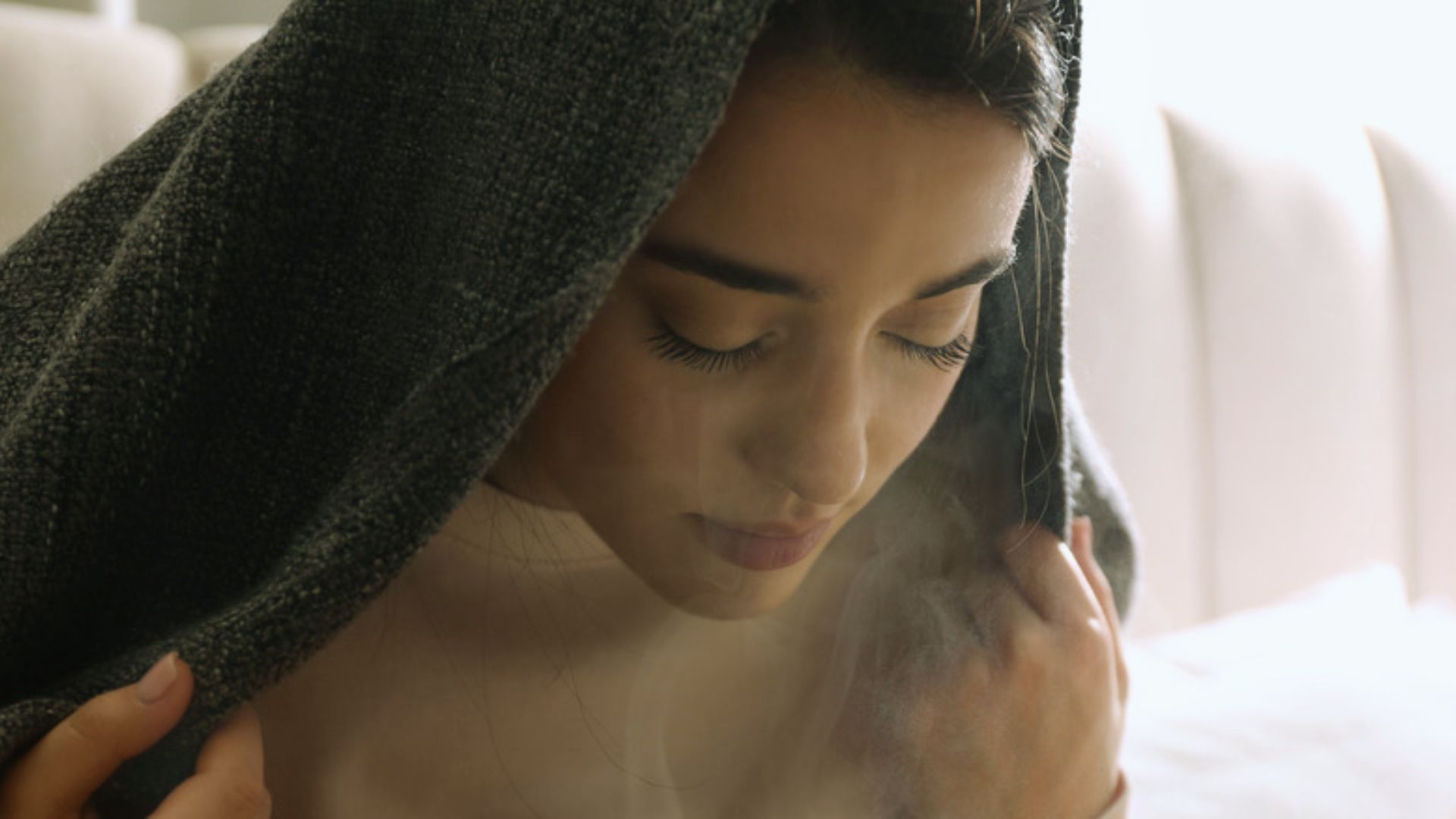 A woman wrapped in a blanket is smoking, appearing relaxed in a cozy indoor setting.