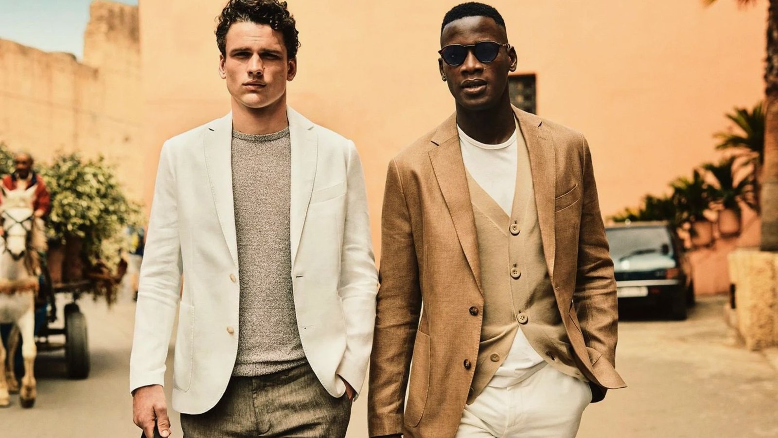 Two men in white suits standing side by side, both smiling and looking towards the camera.