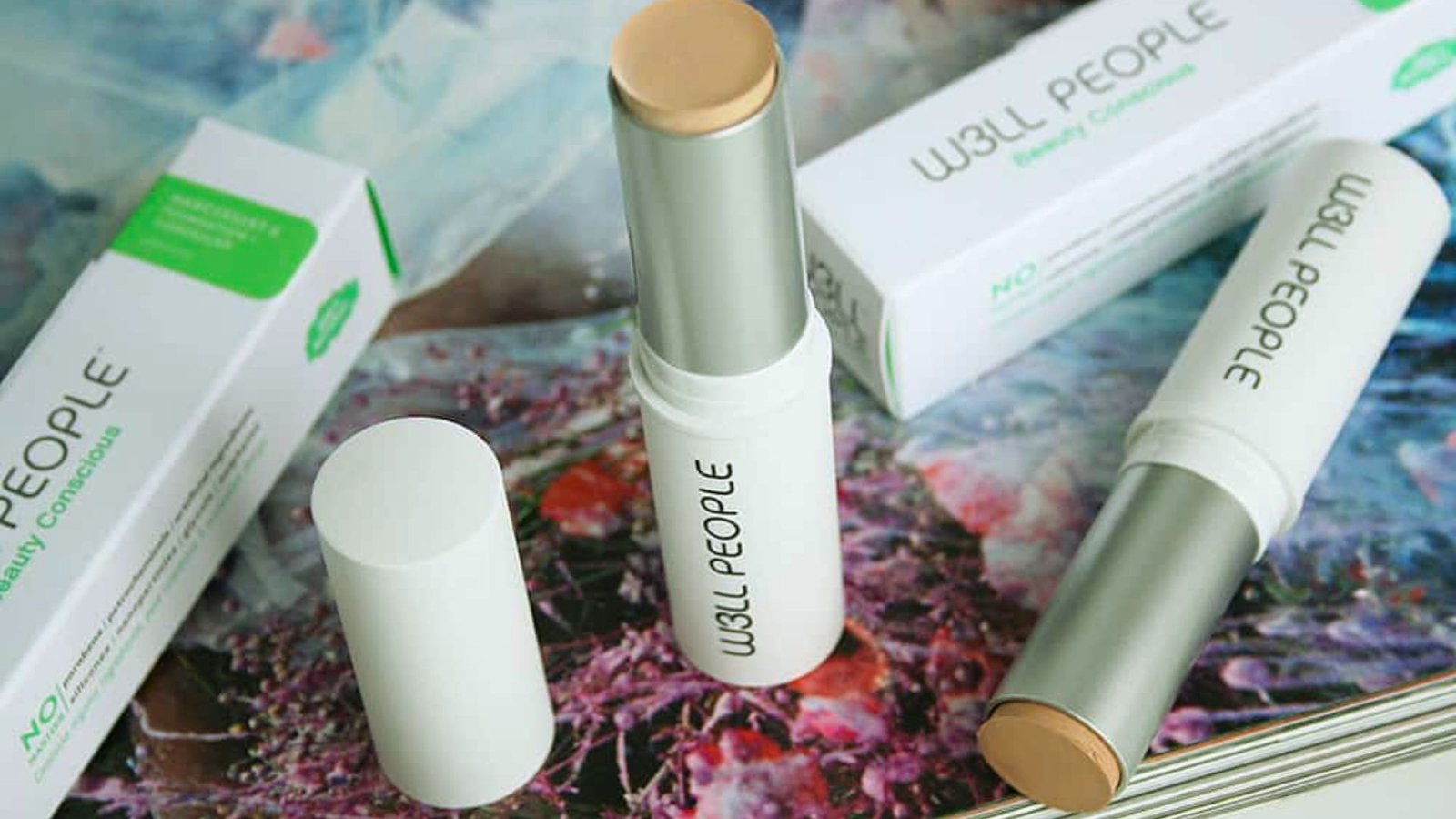 Two tubes of makeup sit on a table beside a box of assorted cosmetics.