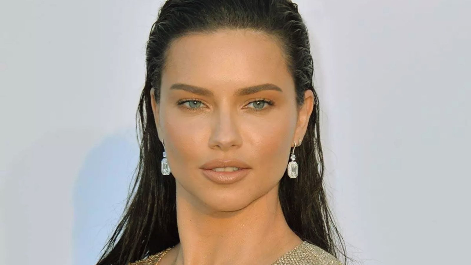 A woman with long hair wearing a shimmering gold dress stands elegantly.