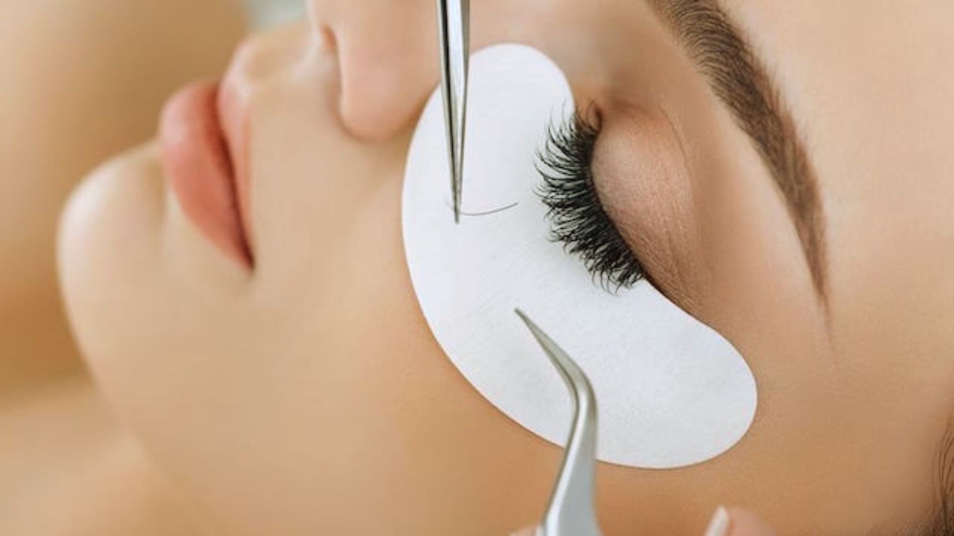 A woman having her eyelashes carefully trimmed with scissors by a beautician in a well-lit salon.